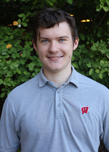 Andrew Beck stands outside smiling, wearing a polo shirt against a green background.