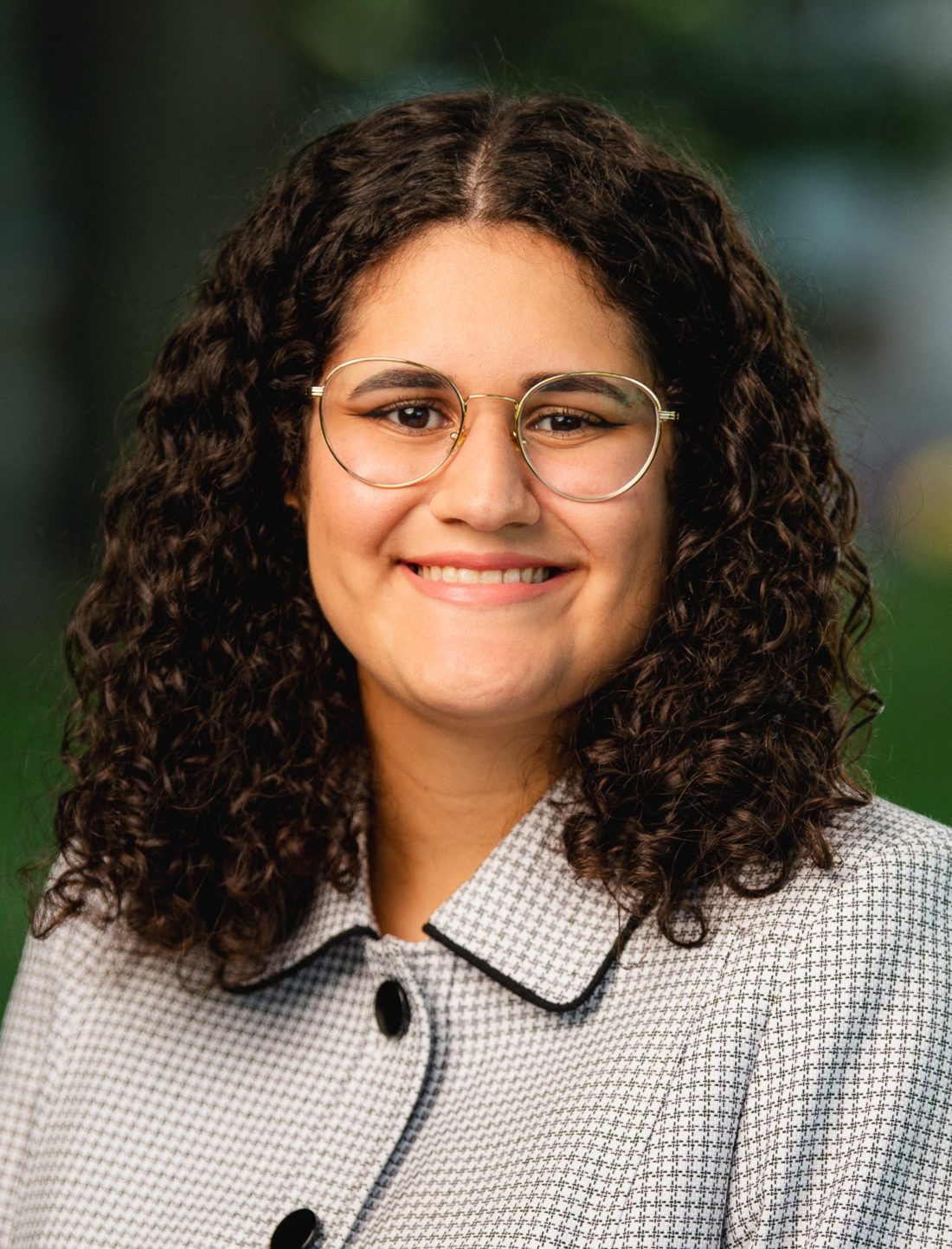 Nadja Aldarondo Quiñones stands outside, looking into the camera and smiling.