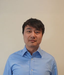 Yihan stands in front of a white background with a blue button-up shirt on.