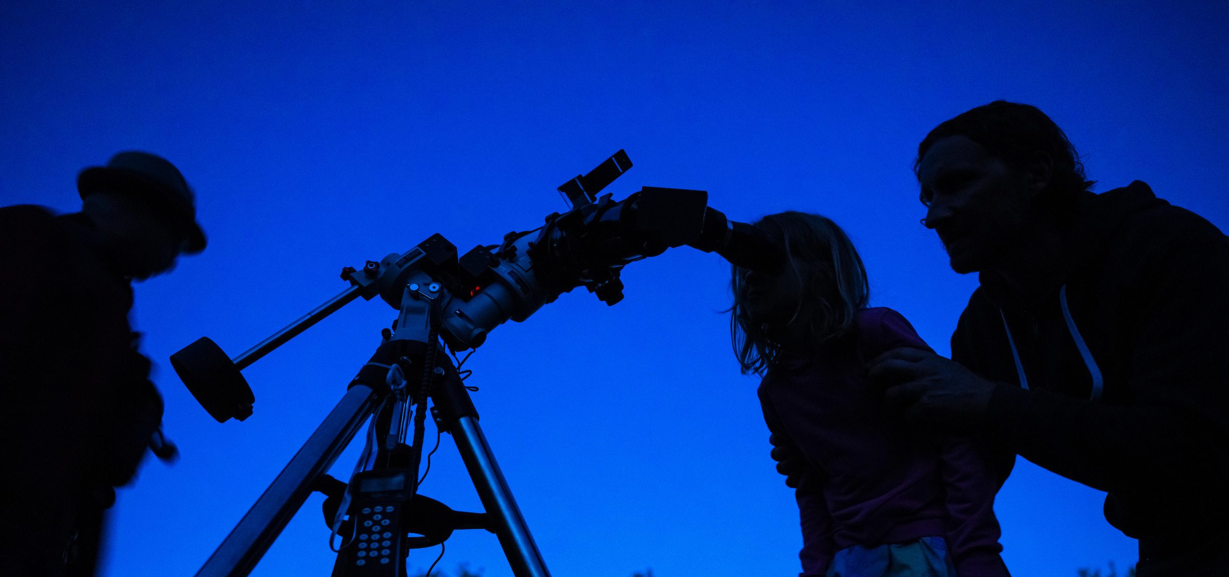 Silhouettes of people viewing the night sky through a telescope at Universe in the Park.
