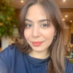 Kaylan Marie Achong smiles for a selfie in a blue shirt.