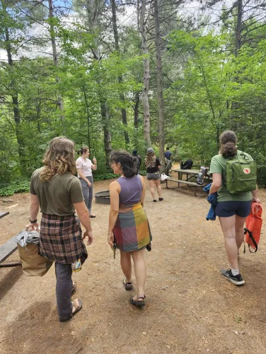 RADIAL students stand outdoors with their back to the camera. A group is gathered on a path in the woods.