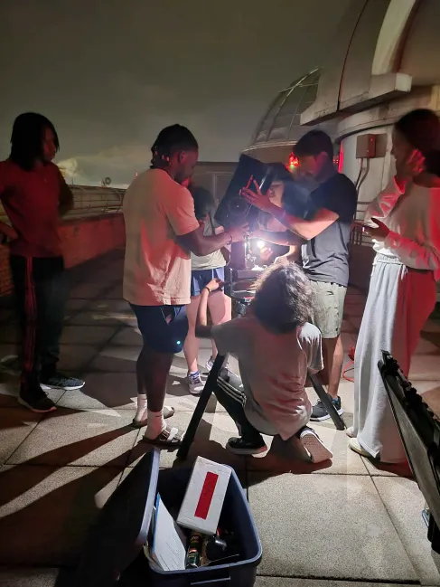RADIAL students gather around a telescope on the roof of Sterling Hall at night.