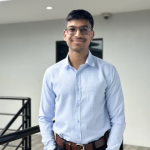 Neval Rattan poses, smiling, for a headshot in a blue button up shirt.