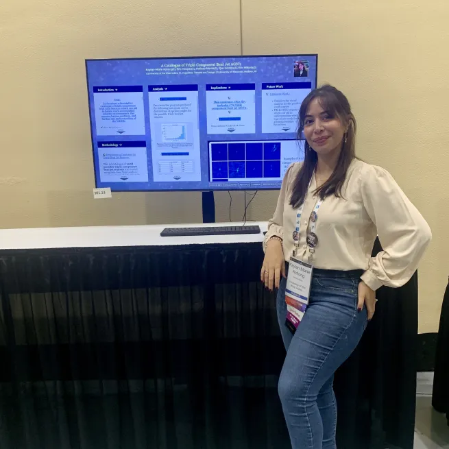 Kaylan Marie Achong stands in front of a poster presentation, smiling with a hand on hip.