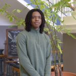Johann Baynes poses for a headshot in front of a large green plant.