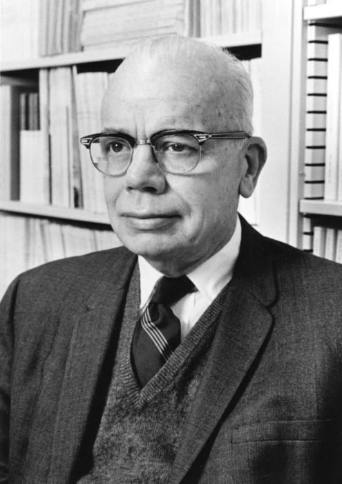 Albert Whitford wears a suit with a library behind him, looking just past the camera.